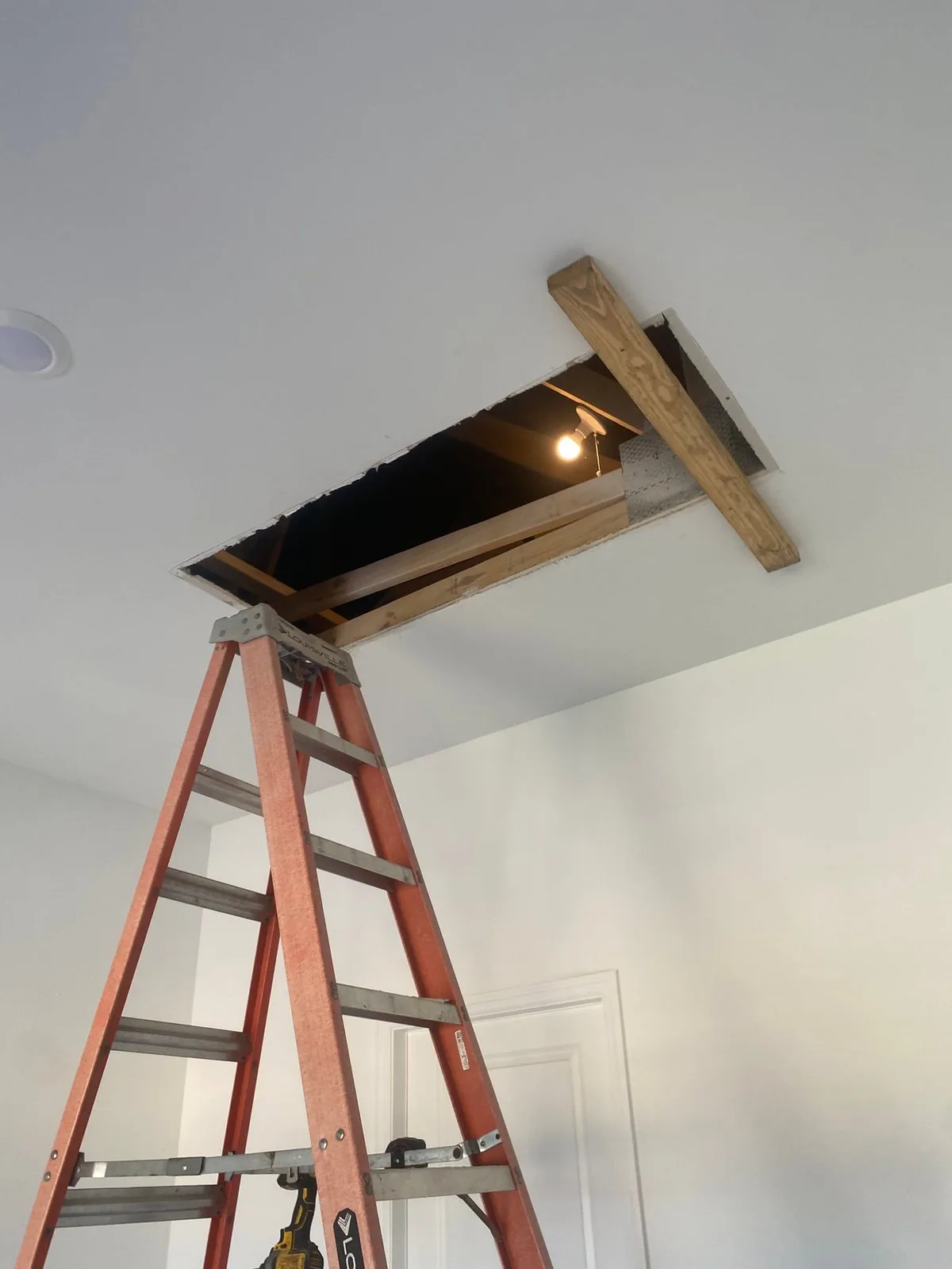 Rectangular opening in a white ceiling with wood edges and a ladder below.