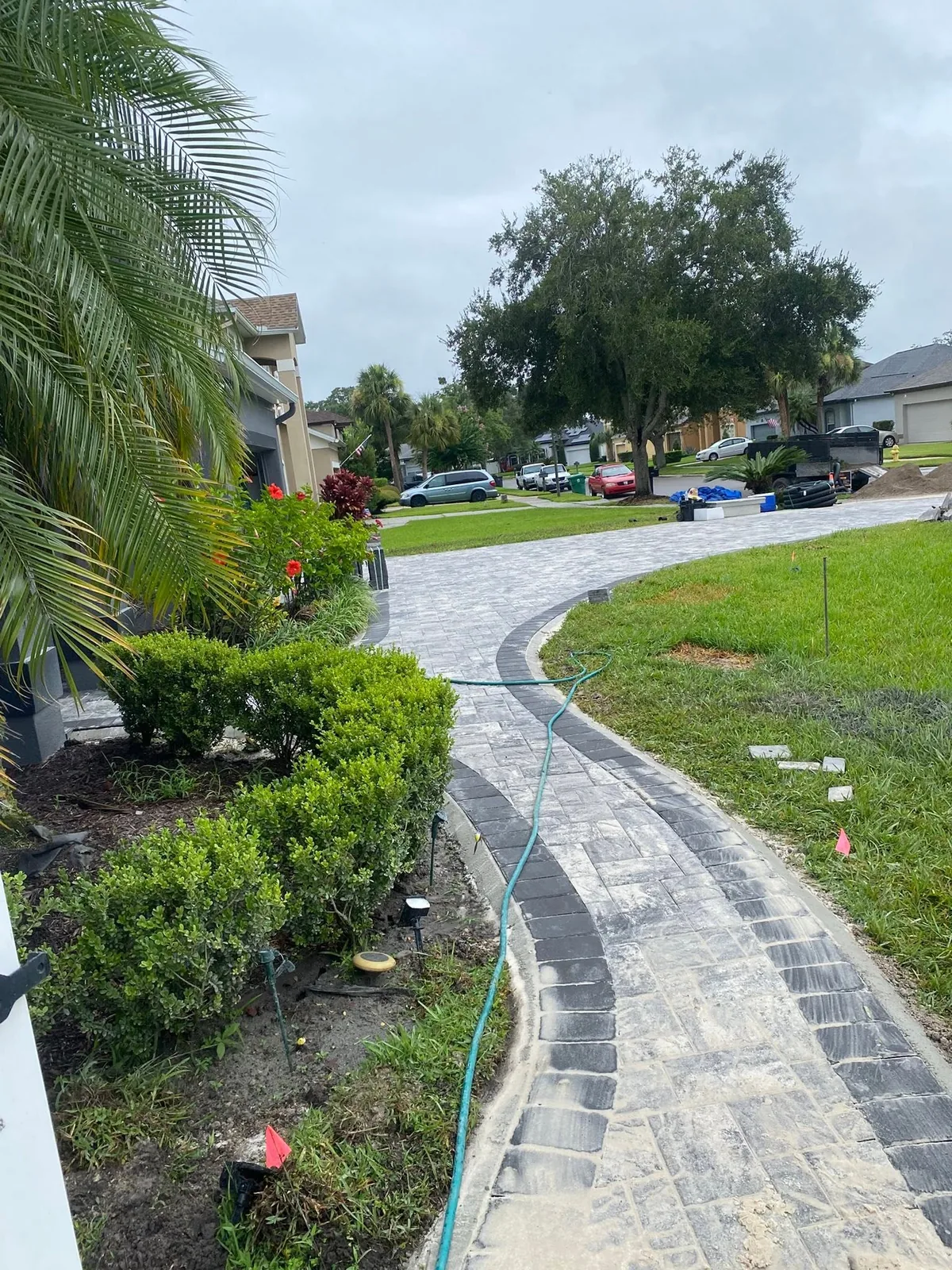 Curved gray paver walkway with a dark border between a planting bed and a lawn.