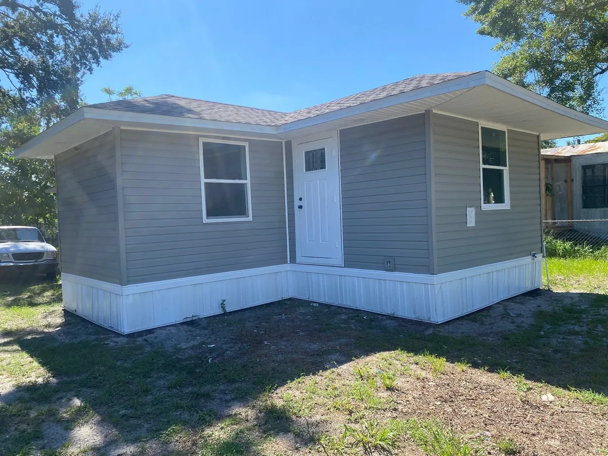 Gray exterior siding with white window trim, a white door and white lower skirting.
