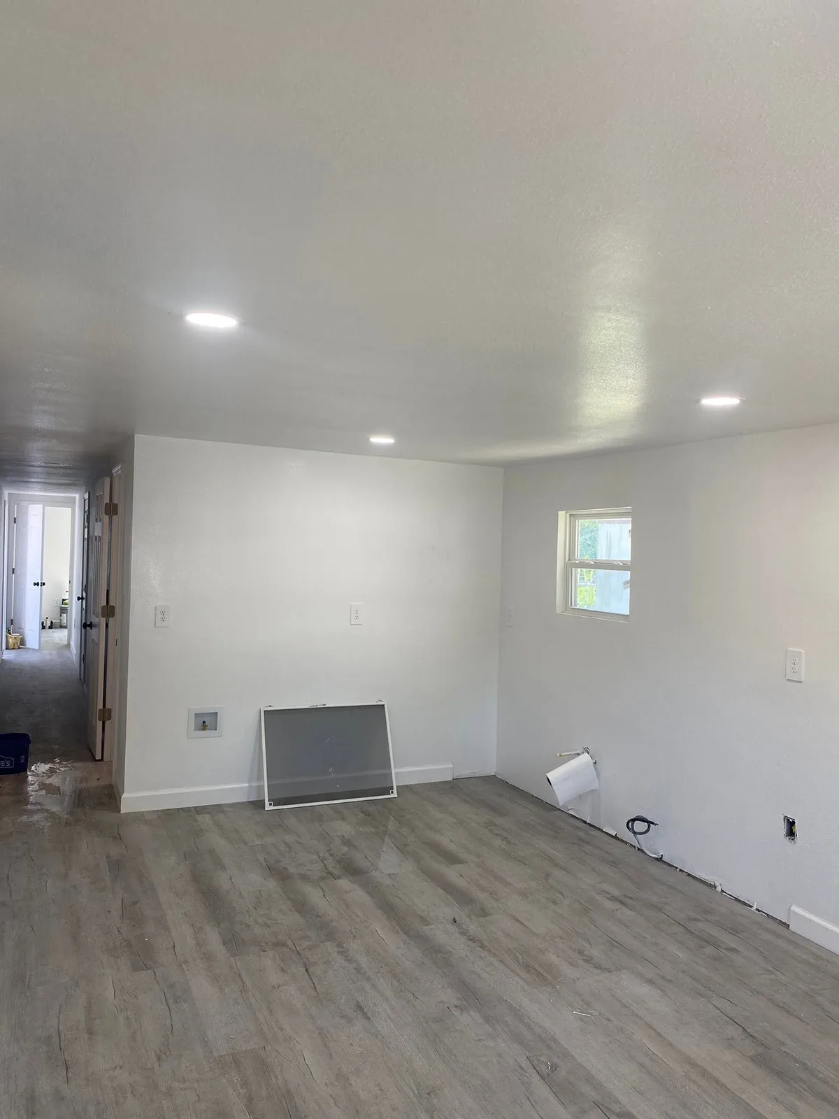 Room with white walls, recessed ceiling lights and gray wood-look flooring.